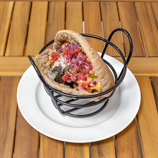 Falafel Taco pita, overflowing with diced tomatoes, red onions, and sauce, in a black wire holder.