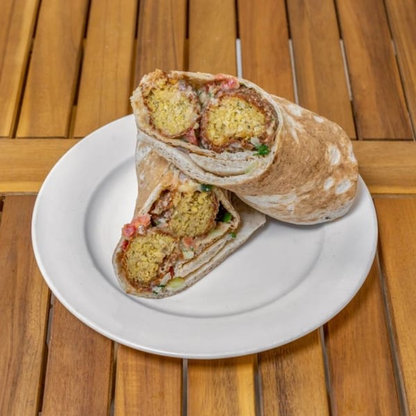 Two Falafel Taco wraps, cut in half, revealing falafel, vegetables, and sauce on a white plate.