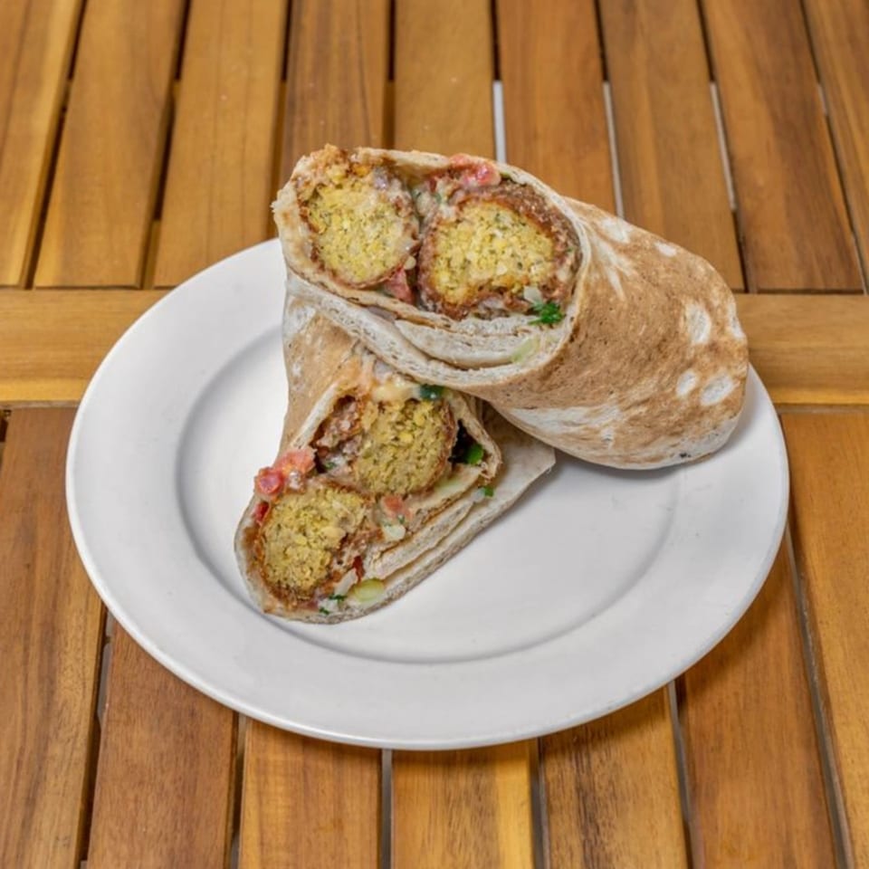 Two Falafel Taco wraps, cut in half, revealing falafel, vegetables, and sauce on a white plate.