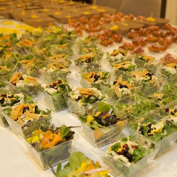 Rows of individual Falafel Taco salads in clear square cups with tortilla strips and dressing.