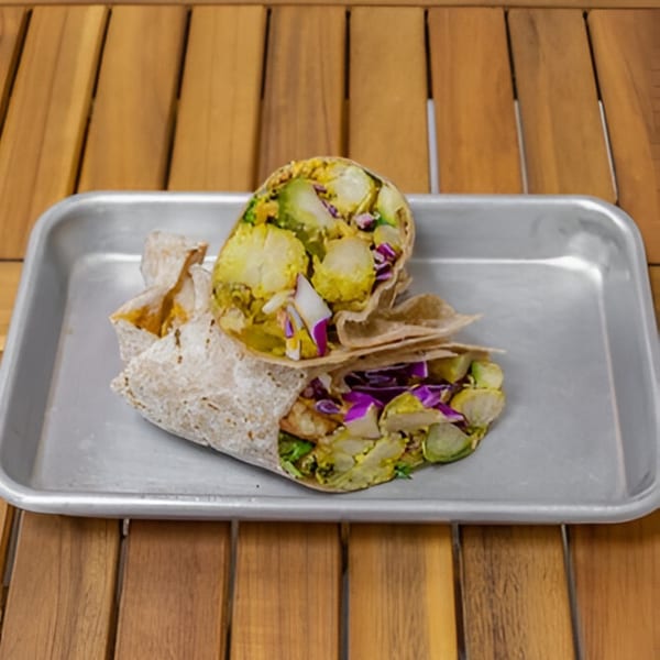 Two Falafel Taco wraps, one cut in half, filled with falafel, cabbage, and avocado on a metal tray.