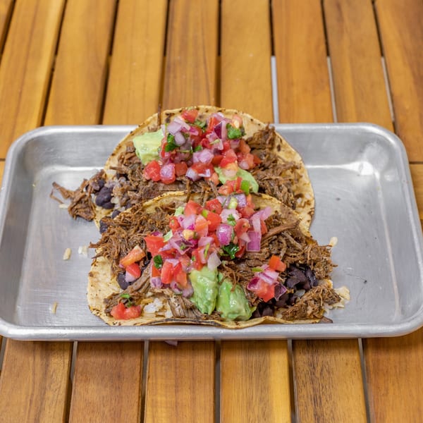 Two Falafel Taco tacos with shredded meat, black beans, rice, guacamole, and pico de gallo.