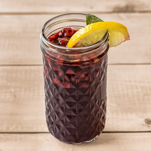 A Falafel Taco pomegranate drink with lemon and mint garnish in a textured glass jar.