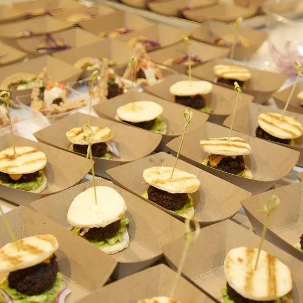 Numerous Falafel Taco sliders with falafel patties, lettuce, and grilled buns in individual paper trays.