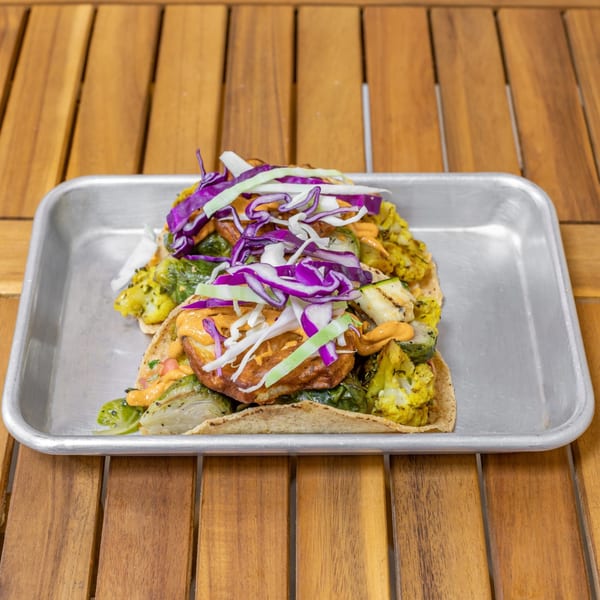 Two Falafel Tacos with roasted vegetables, purple and white cabbage, and orange sauce on a metal tray.
